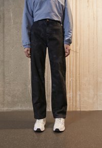 Black denim pants with a straight fit and faded texture, paired with a light blue long-sleeve top and white athletic shoes.