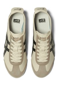 Et par beige og sorte Onitsuka Tiger sneakers med hvide snørebånd vist fra oven på en hvid baggrund.