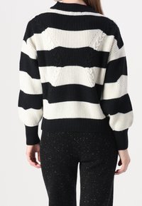 Suéter a rayas negro y crema con textura de canalé, detalles de punto trenzado en la parte posterior y un cuello redondo. Presenta mangas holgadas.