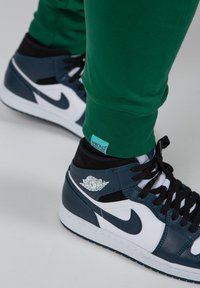Hoge sneakers hebben een navy en witte leren ontwerp met zwarte accenten. Groene sweatpants met een blauwe label zijn zichtbaar nabij de onderkant.