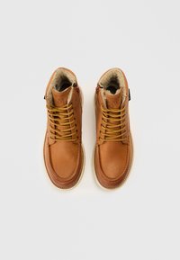 Brune læderankelstøvler med imiteret pelsfor, rundet tå, kontrasterende gule snørebånd og lynlåsdetalje på siden. Holdbar gummisål.