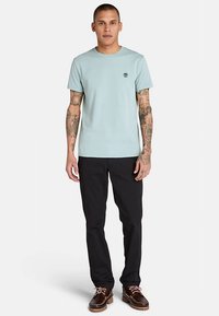 Ljusblå bomulls-T-shirt med korta ärmar och rund halsringning, med en liten rund logotyp på bröstet, kombinerad med svarta byxor.