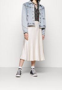 Světlezelená džínová bunda, černý květinový top, krémová saténová sukně a černé vysoké tenisky. Bunda má knoflíkovou přední část a viditelné švy.