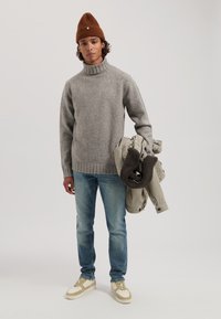 Grijze gebreide trui met hoge hals, lichtblauwe denim jeans en beige sneakers. Houdt een grijze jas vast met bruine fleece voering.