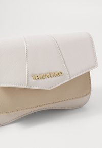 Clutch Valentino in pelle strutturata beige chiaro e bianco sporco, con pattina ripiegata e accentuazione del logo dorato. Finitura liscia, senza hardware visibile.
