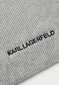 Gorro de malha cinza com nervuras, com bordado preto "KARL LAGERFELD" ao longo da borda inferior, destacando a textura e o design.