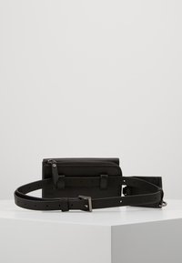 Svart läderväska med avtagbart bälte, med en zippered fack, slät textur och en silverfärgad spänne med flera hål.