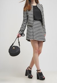Czarno-biała kurtka w paski z dopasowaną spódnicą, teksturowana tkanina, okrągła czarna torebka. Czarne sandały na platformie z paskami wokół kostki.