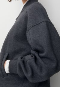 Donkergrijze sweatshirt met een zachte textuur. Voorzien van een rits aan de voorkant, zijzakken en ribgebreide boorden. Eenvoudig ontwerp en een klassieke pasvorm.