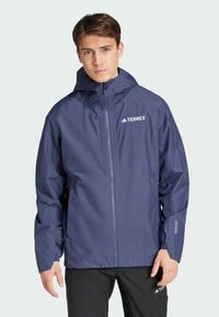 Veste imperméable bleu marine avec capuche, fermeture éclair, poignets élastiques et logo Terrex sur le devant et les manches. Matériau léger.
