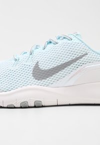 Jasnoniebieskie siatkowe sneakersy z białą podeszwą, wyposażone w wyraźny szary znak Nike, teksturowaną cholewkę oraz regulowane sznurowanie.