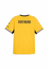 Κίτρινη φανέλα ποδοσφαίρου της Borussia Dortmund με μαύρο κείμενο «DORTMUND» στην πλάτη και μανσέτες με μαύρο-λευκές ριγέ λεπτομέρειες στα μανίκια.