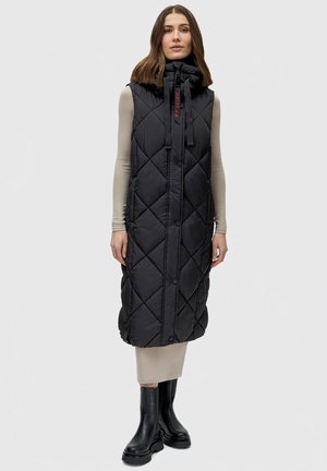 Gilet rembourré noir avec un col haut, un motif en losanges, des boutons sur le devant et un cordon de serrage. Stylisé par-dessus une robe beige et des bottes noires.