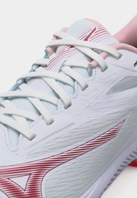 Κοντινό πλάνο ενός λευκού αθλητικού παπουτσιού με κόκκινο λωρίδα λογότυπο, λευκά κορδόνια και εσωτερική επένδυση σε ανοιχτό ροζ χρώμα.