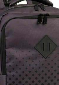 Paarse rugzak van een gestructureerde stof, voorzien van twee zwarte ritsen, een ruitvormig patch en een stippenpatroon langs de onderkant.