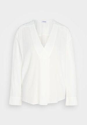 Blusa blanca de manga larga con escote en V y puños con botón. Fabricada en una tela suave con un corte ligeramente holgado y dobladillo redondeado.
