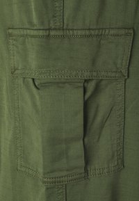 Olive green fabric with a diagonal weave, featuring a flap pocket with reinforced stitching at the upper left side.