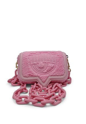 Sac à épaule rose texturé avec motif d'œil embossé et bandoulière chaîne rose brillante épaisse sur fond blanc.