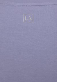 Helllila geripptes Gewebe mit einer subtilen Textur. Im Zentrum befindet sich ein kleines weißes "LA"-Logo innerhalb einer quadratischen Kontur.