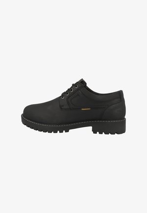 Chaussure en cuir noir avec un bout arrondi, un système de laçage, une tige texturée et une semelle épaisse et robuste présentant des motifs de traction prononcés et des coutures contrastantes.