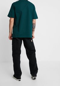 Tee in teal kleur van katoen met een losse pasvorm en korte mouwen, gecombineerd met zwarte cargobroek met zijkanten zakken en een patch-logo.