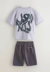 Hele lilla T-särk suure moonutatud musta teksti "ALLSAINTS LONDON" tagaküljel, millele on lisatud tumedat halli värvi elastse vöökohaga püksid tagataskuga.