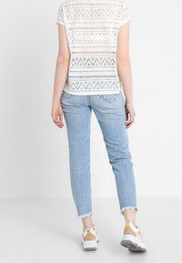 Bílý top s krátkým rukávem a otevřeným vzorem, zkombinovaný se světlomodrými džíny s roztrhaným lemem a bílými teniskami se žlutými akcenty.