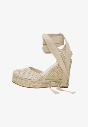 Sandales compensées beige avec dessus en tissu tissé, plateforme espadrille texturée et brides croisées en tissu autour de la cheville pour un maintien sûr.