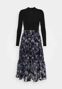 Robe longue avec haut noir uni moulant et col haut, jupe fluide présentant un motif floral superposé noir et gris.