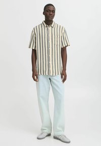 Camicia in tessuto con strisce verticali beige e blu navy, colletto button-down e taschino frontale, abbinata a pantaloni in denim chiaro.