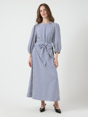 Robe maxi rayée en bleu et blanc. Comprend des manches bouffantes, un décolleté bateau et un détail de taille nouée. Tissu en coton lisse.