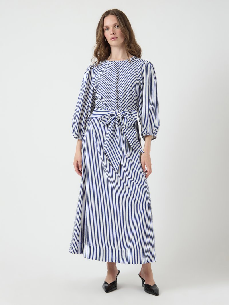 Striped maxi dress in blue and white. Features puffed sleeves, a bateau neckline, and a knotted waist detail. Smooth cotton fabric.