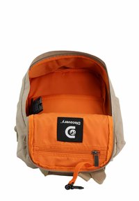 Beige Rucksack mit einem Reißverschluss. Innen hat er ein orangefarbenes Futter und eine rechteckige Tasche. Markenlabel im Taschenbereich sichtbar.