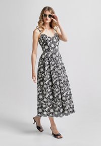Rochie maxi floral alb-negru cu decolteu și tiv ondulat. Prezintă bretele subțiri și un corset ajustat, asortată cu sandale negre cu toc.