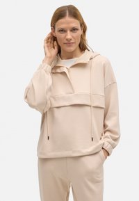 Pullover beige claro con capucha, presenta un cuello con media cremallera, bolsillo frontal y puños elásticos. Material suave con una textura lisa.