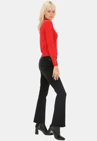 Czerwony dopasowany sweter o prążkowanej teksturze z guzikami na rękawach, w połączeniu z czarnymi spódnicami dzwonowymi i botkami za kostkę.