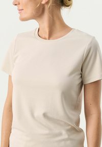 T-shirt beige a maniche corte realizzato in tessuto morbido con scollatura rotonda e design aderente, che mostra una silhouette semplice e classica.