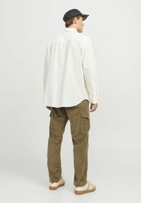 Light-colored striped shirt, olive corduroy cargo pants, beige sandals, black cap, showing back view of the outfit.