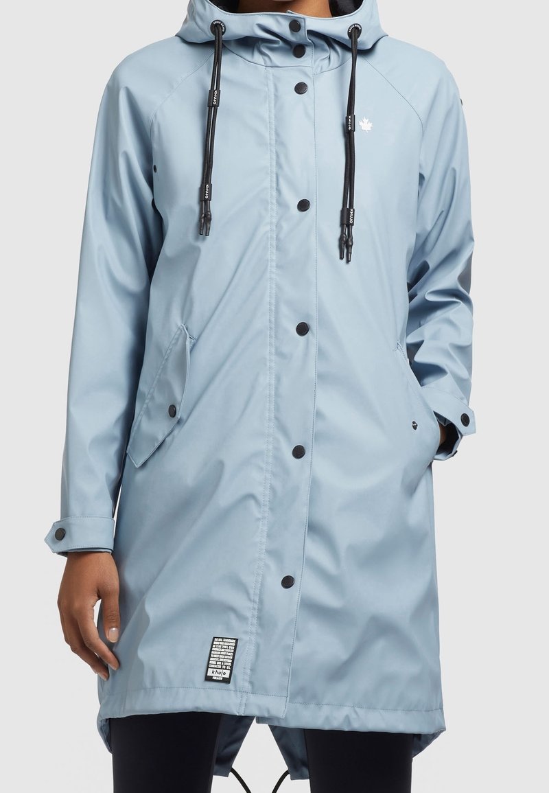 Impermeabile azzurro chiaro con cappuccio, realizzato in materiale impermeabile. Presenta bottoni a pressione neri, cordini regolabili e tasche laterali.