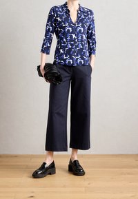 Blusa de estampado marino con mangas de tres cuartos, combinada con pantalones anchos marinos y zapatos de charol negros gruesos, sosteniendo un clutch negro texturizado.