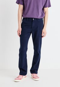 Navy blue cotton trousers with a straight fit, featuring a button closure and belt loops, paired with a purple T-shirt and pink sneakers.