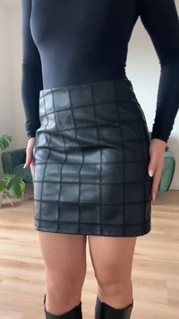 Juodos dirbtinės odos mini sijonas su kvadratinių raštų siuvinėtu raštu; lygi tekstūra ir aptempta forma.