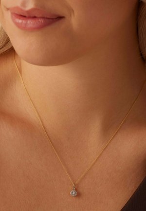 Gouden ketting met een ronde hanger met een cluster van fonkelende heldere kristallen, rustend op gladde huid.