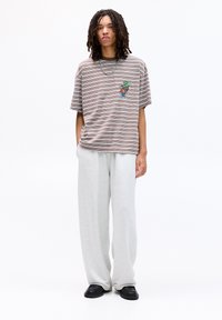 Brun og beige stribet T-shirt med en lille farverig grafik på venstre bryst, kombineret med grå sweatpants og sorte sko.