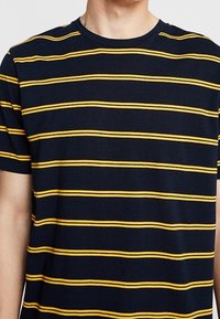 Camiseta de manga corta azul marino con rayas amarillas horizontales, escote redondo y una textura de tela suave. Diseño sencillo sin adornos.