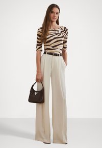 Camisola de malha às riscas em castanho e creme, calças de cintura alta em bege claro e uma mala castanha escura com detalhes em metal prateado.