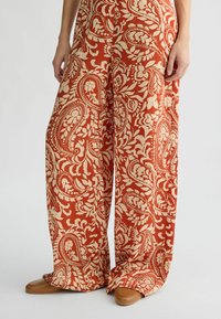 Brede broekspijpen in een roest-oranje stof met een off-white paisley- en bloemenpatroon, met een soepele textuur en een ontspannen pasvorm.