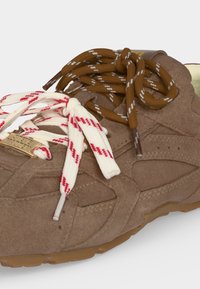 Baskets en daim marron avec deux jeux de lacets : un blanc à rayures rouges, un marron à rayures blanches, noués en nœuds lâches.