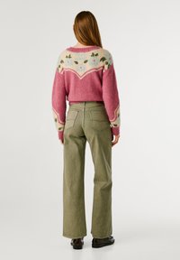 Suéter de punto rosa con un patrón floral sobre un fondo crema, combinado con pantalones de pierna ancha en un ligero tono verde oliva. Textura suave, ajuste casual.