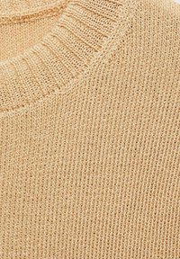 Beige knitted sweater fabric with a ribbed neckline, featuring a loose, textured weave and subtle horizontal lines throughout.